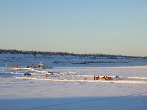 The ice bridge crew on the Arctic Red River ice bridge, with the ferry and excavators in the background keeping the Mackenzie River crossing open